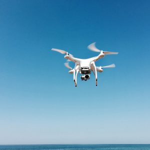 photo of a white drone in flight with a camera mounted underneath